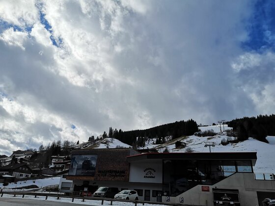 Moderne Talstation der Wagstättbahn in Jochberg vor verschneitem Berghang unter bewölktem Himmel.