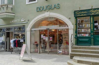 Douglas Filiale in der Innenstadt Eingangsbereich einer Douglas-Filiale in einer Fußgängerzone neben einem Lacoste-Shop und einer Buchhandlung.