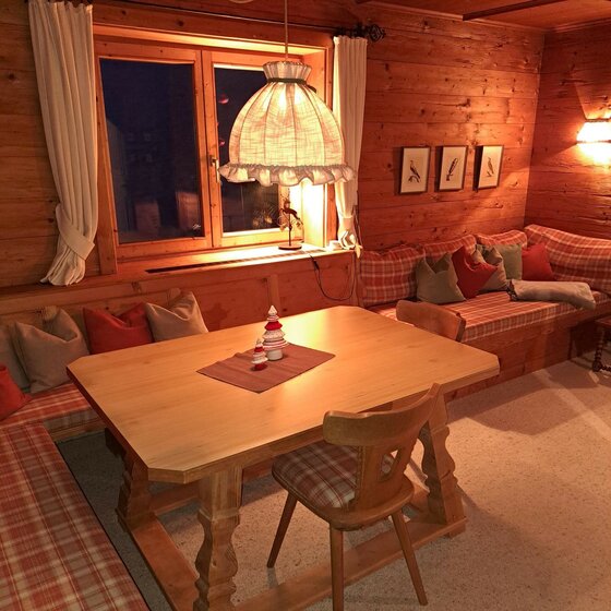 Schatzhof Wohnzimmer Rustikale Sitzecke aus Holz mit Esstisch, Eckbank und einer Hängelampe in einer holzgetäfelten Stube.
