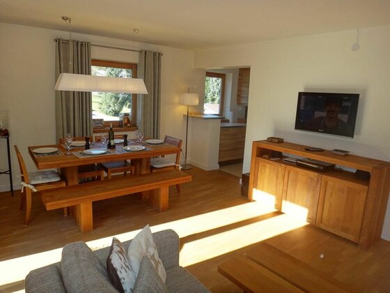 Essbereich Apartment Panorama Moderner Essbereich aus Holz mit gedecktem Tisch, Sitzbank und angrenzendem Wohnzimmer mit TV.