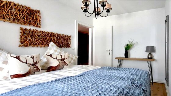 Schlafzimmer Belle Kitz Pure Modernes Schlafzimmer mit Doppelbett, Kissen mit Hirschmotiven und Wanddekoration aus Holzästen.
