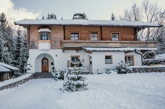 Zweistöckiges Alpenhaus mit Holzfassade und weißem Erdgeschoss in einer verschneiten Winterlandschaft.