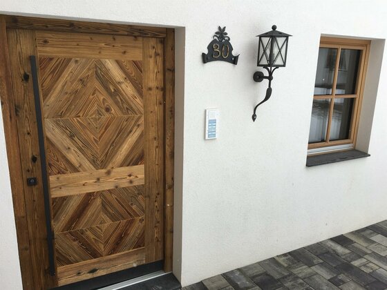 Eingangsbereich Bauernhof Froidl Eingangsbereich eines Hauses mit gemusterter Holztür, Hausnummer 30, Außenleuchte und Fenster.