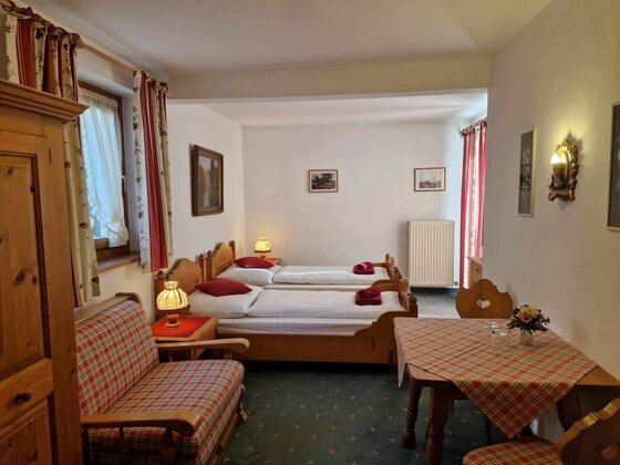 Gästezimmer mit zwei Einzelbetten aus Holz, einer Sitzecke und einem Tisch mit karierter Decke.