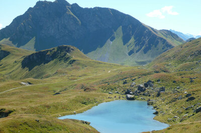 Torsee mit Bergpanorama Ein blauer Bergsee in einer grünen Almlandschaft vor einem hohen Felsmassiv.