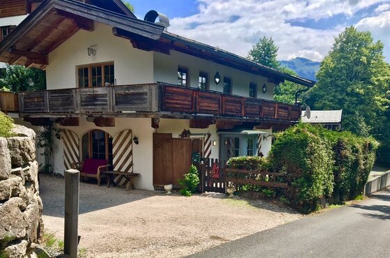 Aussenansicht Chalet Belle Kitz Zweistöckiges alpines Gebäude mit Holzbalkon, weißer Fassade und Fensterläden vor Bäumen.
