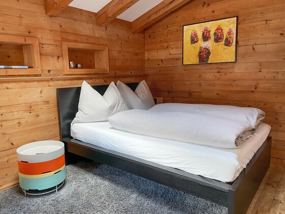Schlafzimmer mit Doppelbett in einer holzgetäfelten Hütte.