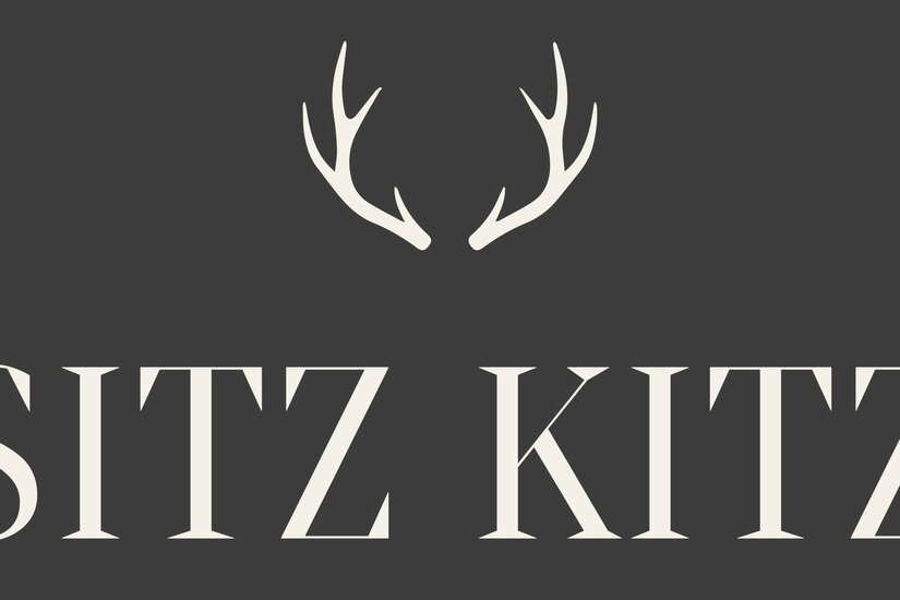 Sitz Kitz Logo Logo mit weißem Geweih-Symbol und dem Schriftzug SITZ KITZ auf dunkelgrauem Hintergrund.
