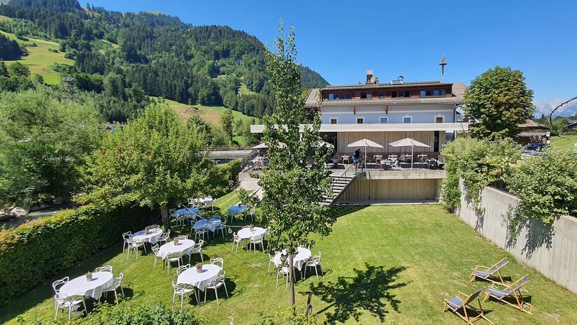 Außenansicht Gasthof Auwirt Außenbereich des Gasthof Auwirt mit gedeckten Tischen auf einer Wiese vor dem Gebäude und bewaldeten Bergen.