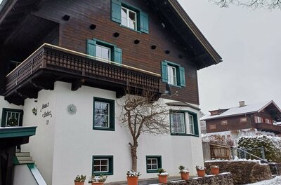 Zweistöckiges alpines Wohnhaus mit dunkler Holzfassade im Obergeschoss und weißem Putz im Erdgeschoss.