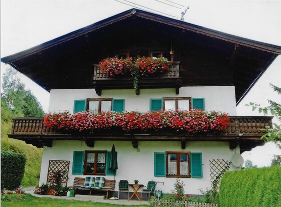 Haus Alpenrose Alpenländisches Wohnhaus mit zwei blumengeschmückten Holzbalkonen und grünen Fensterläden.