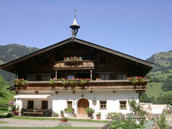 Malernhof Kitzbühel Ansicht Traditionelles Alpenhaus aus Holz und Stein mit Blumenschmuck vor Bergen.