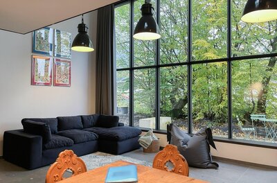 Moderner Wohnbereich im Loft Moderner Wohnraum mit dunklem Sofa, Holztisch und großer Fensterfront zum Garten.