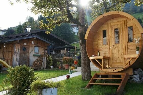 Garten mit Fasssauna Eine hölzerne Fasssauna im Garten neben einer rustikalen Holzhütte unter Bäumen.