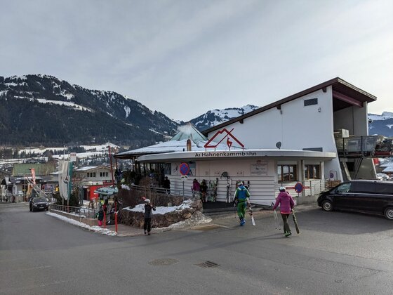 Talstation der Hahnenkammbahn mit Skifahrern vor schneebedeckten Bergen.