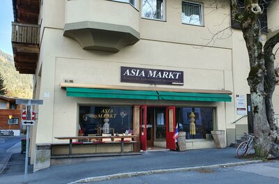 <p>Ein asiatischer Markt mit einem Schaufenster und einer rot lackierten Tür. Vor dem Geschäft stehen ein Fahrrad und einige Produkte sind ausgestellt.</p>