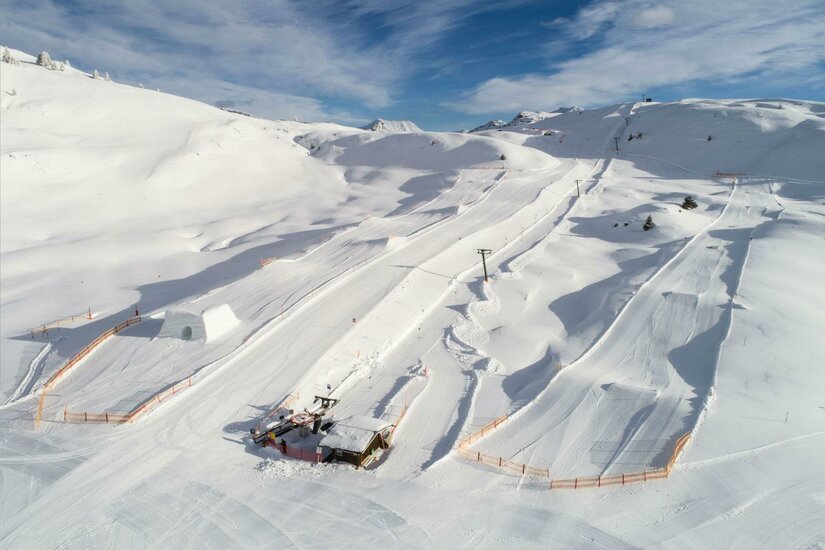 SnowparkHorn Eine schneebedeckte Landschaft mit Skihängen und einem kleinen Skilift. Der Himmel ist klar und blau, ideal für Wintersport.