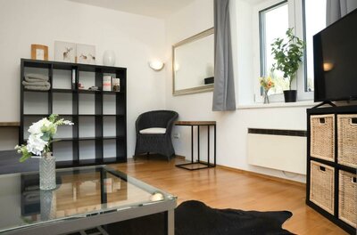 587402277 Ein modernes Wohnzimmer mit einem gläsernen Tisch, einem schwarzen Regal und einem Sofa. Große Fenster lassen viel Licht herein und sorgen für eine einladende Atmosphäre.