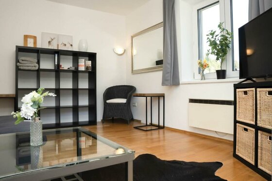 587402277 Ein modernes Wohnzimmer mit einem gläsernen Tisch, einem schwarzen Regal und einem Sofa. Große Fenster lassen viel Licht herein und sorgen für eine einladende Atmosphäre.