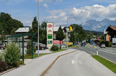 Fachmarktzentrum Bushaltestelle Blick auf eine Bushaltestelle und einen Gehweg vor einem Fachmarktzentrum mit Bergpanorama im Hintergrund.