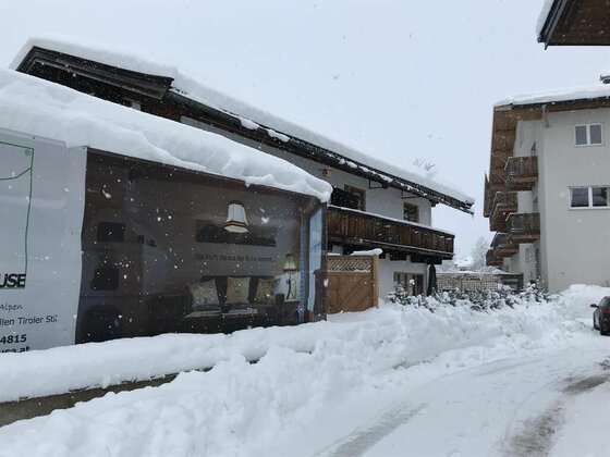 Verschneite Gebäude mit hohen Schneelasten auf den Dächern und einer geräumten Straße im Vordergrund.