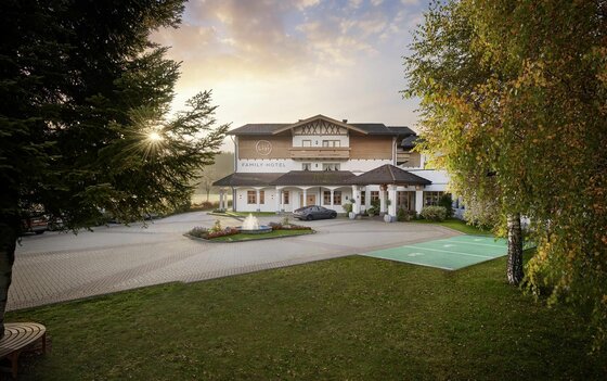 Außenansicht des Lisi Family Hotels mit gepflastertem Vorplatz, Springbrunnen und Bäumen bei Sonnenuntergang.