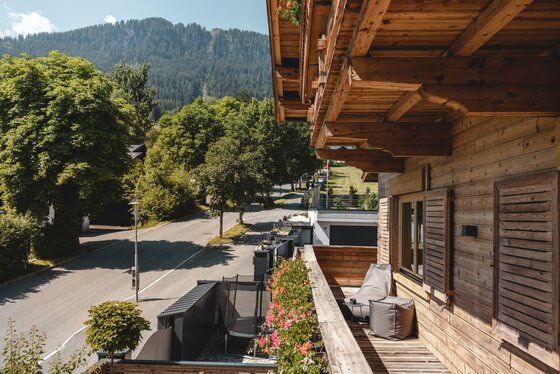 Balkon des Ferienappartements Holzbalkon mit Sitzsäcken und Blick auf eine Straße sowie bewaldete Berge.