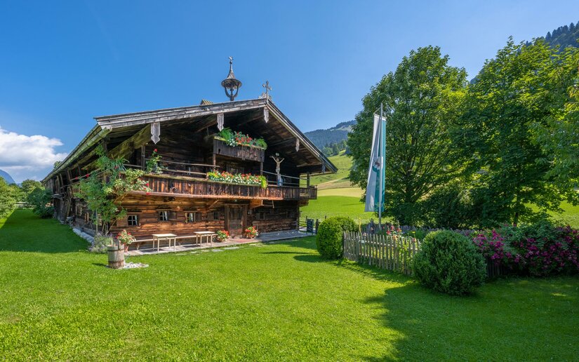 Bauernhausmuseum 1 Ein charmantes Holzhaus umgeben von grünem Rasen und Bäumen. Der blaue Himmel und die idyllische Landschaft schaffen eine ruhige Atmosphäre.