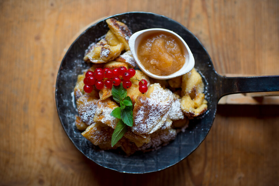 Ein rustikales Gericht aus Kaiserschmarrn, garniert mit roten Johannisbeeren und frischer Minze, serviert mit Apfelmus.