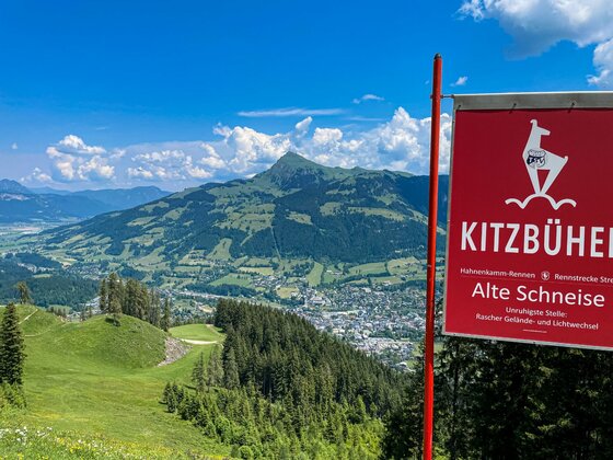 Streif Alte Schneise Rotes Hinweisschild der Kitzbüheler Streif mit Blick auf bewaldete Berge und das Tal im Sommer.