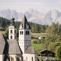 Im Vordergrund stehen historische Kirchengebäude, während die Alpen im Hintergrund eine atemberaubende Kulisse bieten.