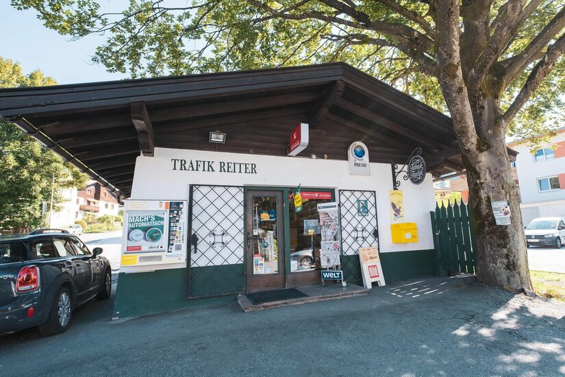 Trafik Reiter Außenansicht Außenansicht der Trafik Reiter in einem flachen Gebäude mit dunklem Holzdach und Zeitungsständern vor dem Eingang.