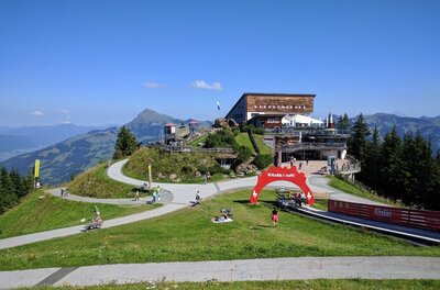 Berghaus am Hahnenkamm Berghaus auf einem Gipfel mit befestigten Wanderwegen und einem roten Torbogen unter blauem Himmel.