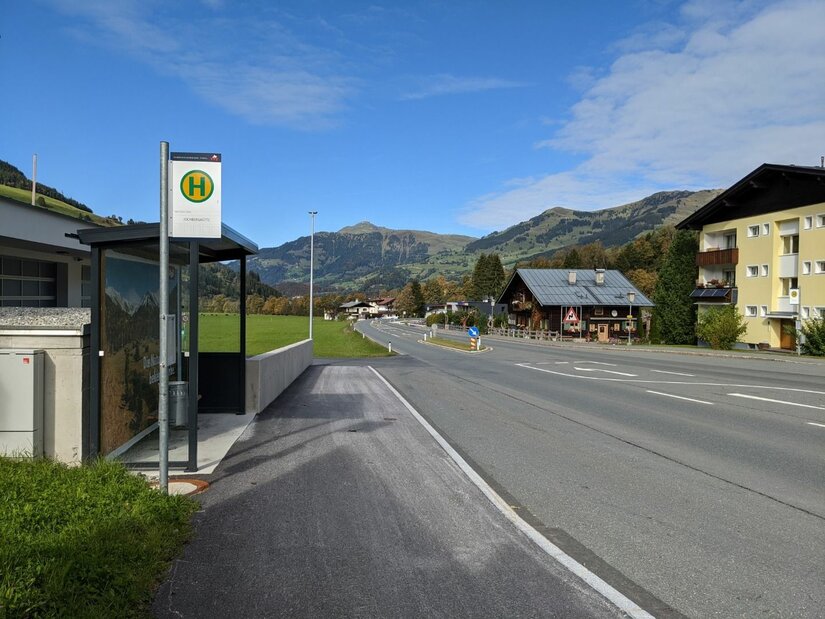 Bushaltestelle an einer Landstraße mit Bergen im Hintergrund.
