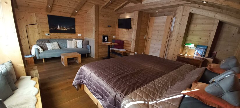 Ein gemütliches Zimmer mit Holzwänden und einem großen Bett. Die Einrichtung ist modern und einladend, mit einem Sofa und einem Fernseher.