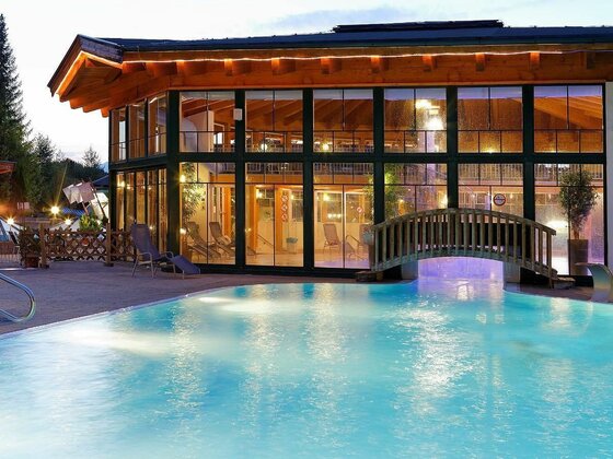 Ein schöner Pool vor einem modernen Gebäude mit großen Fenstern. Die entspannte Atmosphäre wird durch die sanfte Beleuchtung am Abend unterstrichen.