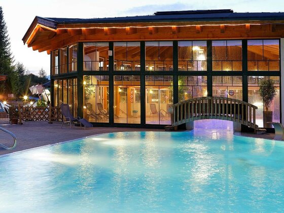 Ein schöner Pool vor einem modernen Gebäude mit großen Fenstern. Die entspannte Atmosphäre wird durch die sanfte Beleuchtung am Abend unterstrichen.
