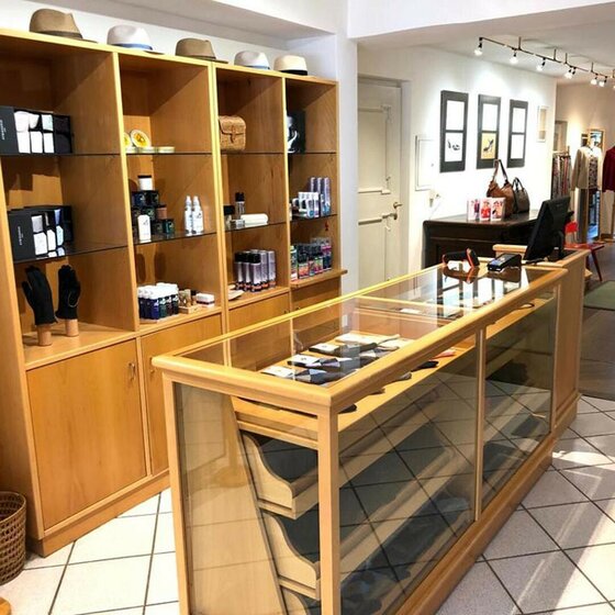 Innenansicht eines Verkaufsraums mit Holzregalen, einer Glasvitrine als Tresen und verschiedenen Accessoires.