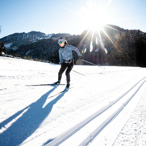 During a cross-country skiing event in Kitzbühel, a skier glides across the snow-covered landscape in the bright sunshine.