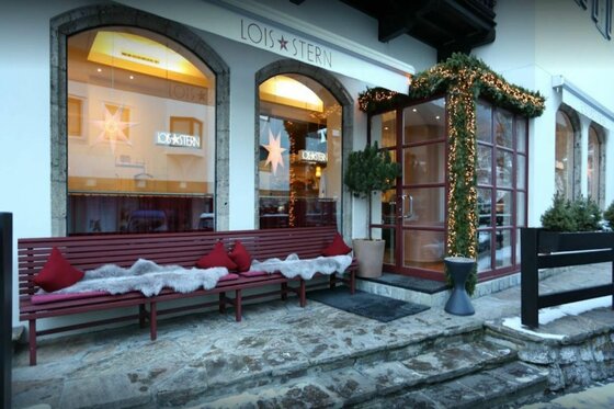 Lois Stern Winter Außenansicht des Restaurants Lois Stern mit einer Holzbank, Fellen und Weihnachtsdekoration.