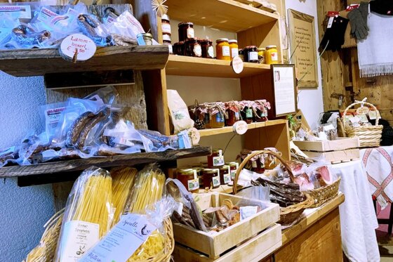 Ein Regal mit verschiedenen regionalen Lebensmitteln, darunter Pasta, Marmelade und Snacks. Die Ware ist liebevoll präsentiert und verstärkt den rustikalen Charme des Geschäfts.