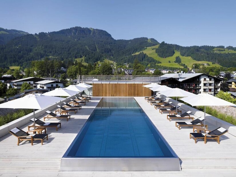 Dachpool Hotel Schwarzer Adler Ein langer Außenpool auf einer Dachterrasse mit Liegestühlen, Sonnenschirmen und Blick auf bewaldete Berge.