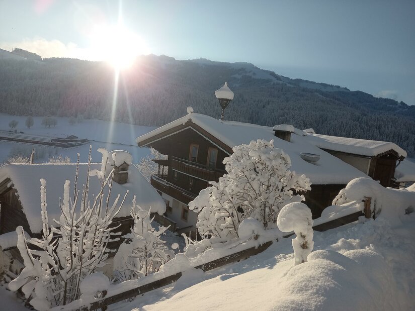 Verschneite Holzhäuser in einer alpinen Winterlandschaft bei tiefstehender Sonne.
