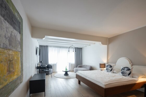 Modernes Hotelzimmer mit Doppelbett, Holzboden, Schreibtisch und Sitzecke vor einem hellen Fenster.