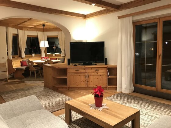 Wohnbereich Apartment Hahnenkammblick Wohnzimmer mit Holzmöbeln, Fernseher, Couch und angrenzender Essecke in einer Ferienwohnung.
