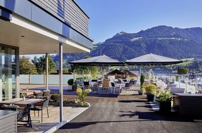 Außenterrasse des Aktivhotel Schweizerhof mit Tischen, Sonnenschirmen und Blick auf die Kitzbüheler Alpen.