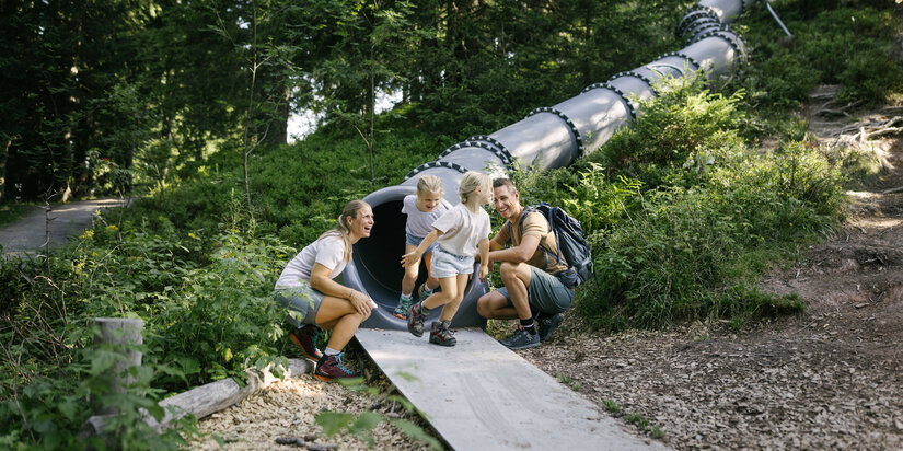 Sommerliches Streiferlebnis: Eltern beobachten spielende Kinder im Wald in Kitzbühel.