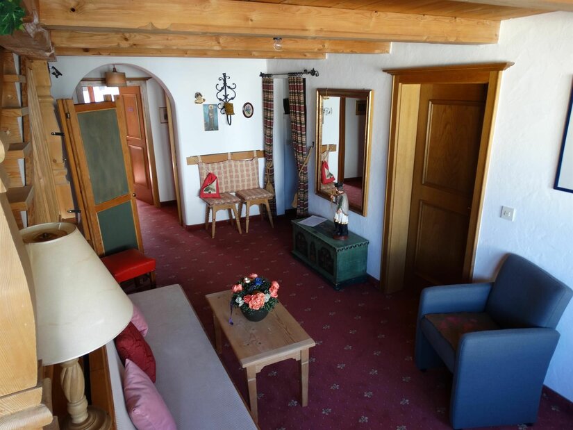 Rustikaler Wohnraum mit Holzbalkendecke, Sofa, Sessel und rotem Teppichboden.