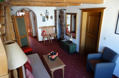 Rustikaler Wohnraum mit Holzbalkendecke, Sofa, Sessel und rotem Teppichboden.