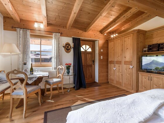 Innenansicht Appartement Das Chalet Rustikales Zimmer mit Holzdecke, Esstisch, Kleiderschrank und Fernseher.